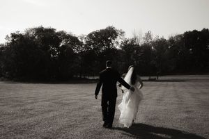 A couple walks through an open field at sunset in black and white photography.