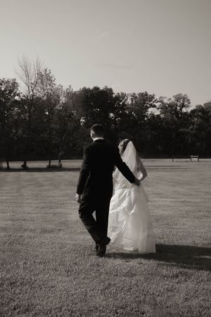 Wedding couple strolls across a grassy field in monochrome.