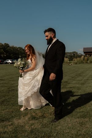 Couple walks through grassy field during outdoor wedding photo session at sunset.