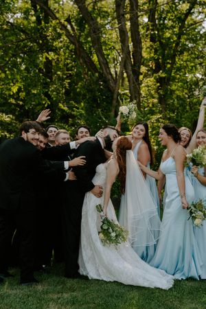 Wedding party poses playfully on grass in light blue bridesmaid dresses.