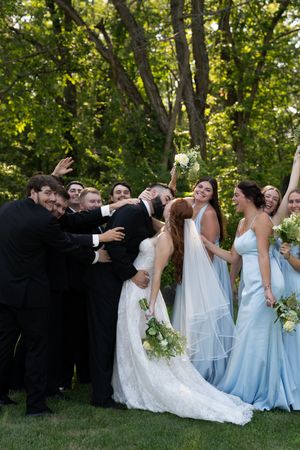 Wedding party shares candid laughing moment during outdoor photo session in wooded setting.