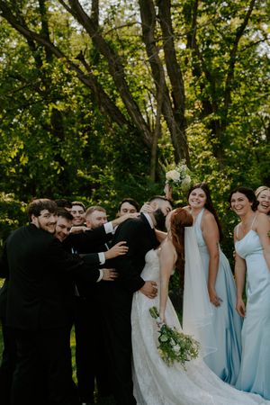 Bridal party laughs together during outdoor photo session with bridesmaids in pale blue dresses.