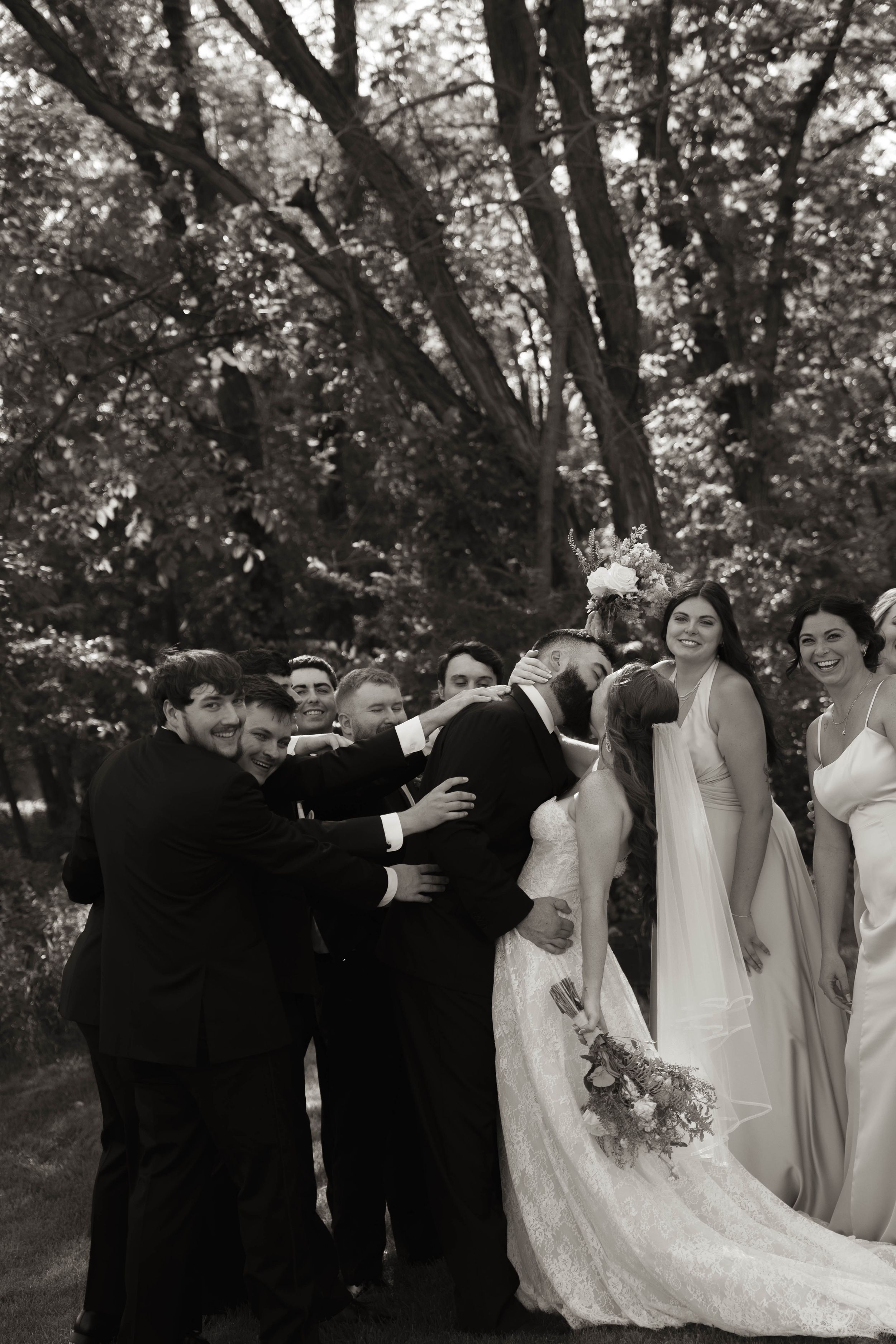 Wedding party poses together outdoors with bridesmaids in light dresses and groomsmen in dark suits.