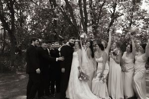 Black and white photo of wedding party celebrating outdoors with raised arms.