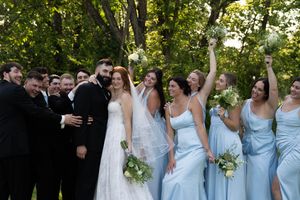 Wedding group poses for candid shots in a wooded outdoor setting wearing blue and black formal attire.