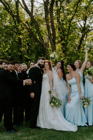 Bridal party in light blue dresses and black suits poses for casual photos in a natural outdoor setting.