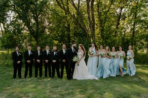 Wedding party poses casually on grass with trees creating natural backdrop.
