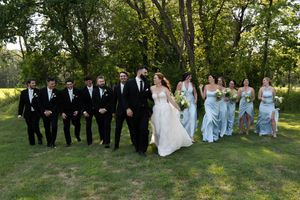 Large bridal party arranged for formal group photos outdoors with natural greenery background.