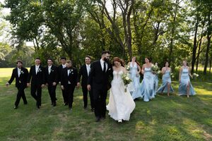 Wedding party poses on grass with bridesmaids in light blue dresses and groomsmen in black tuxedos.