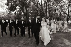 Black and white photo of wedding party walking together on grassy outdoor path.