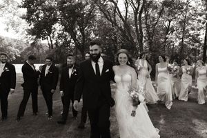 Wedding party poses outdoors under trees for group photos.