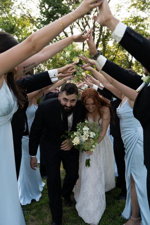 Wedding party forms celebratory arch with raised arms as couple walks underneath.