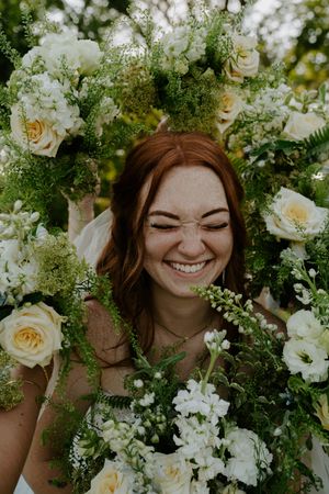 Close up portrait framed by white roses and greenery in natural outdoor setting.