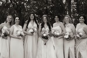 Bridesmaids in light colored dresses pose together holding bouquets.