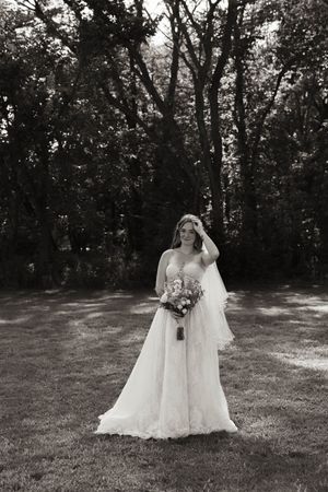 Two brides in white wedding dresses pose together in a sunlit outdoor garden setting.