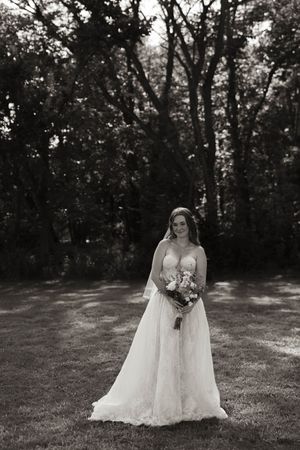 Black and white bridal portrait in a wooded setting with lace dress and bouquet.
