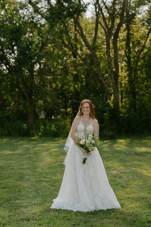 Elegant bridal portraits on grassy hill with natural woodland backdrop.