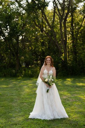 Two brides in white wedding dresses share a joyful moment in a sunlit outdoor setting.