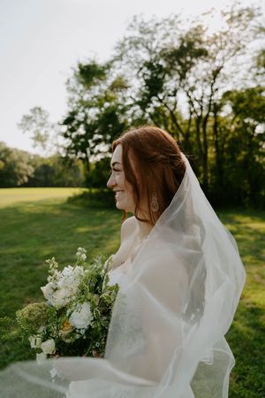 Ethereal bridal portrait with flowing veil and white bouquet in golden evening light.