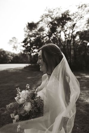 Black and white portrait of bride with flowing veil and bouquet in natural light.