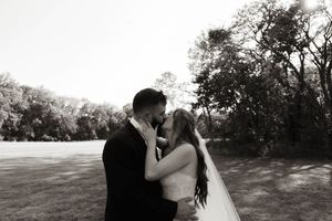 A romantic black and white wedding photo of a couple sharing a kiss in an outdoor garden setting.