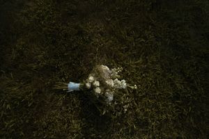 A delicate white bridal bouquet lying on grass in natural lighting.