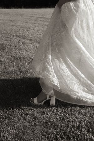 Detail shots of a lace wedding dress hem flowing over grass in black and white.