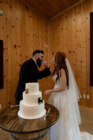 Newlyweds sharing a cake cutting moment at their reception in a wood-paneled venue.