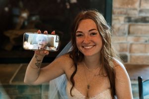 A joyful bride in white holds up her phone during a wedding celebration.