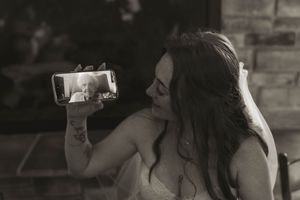 A candid black and white photo of a bride showing something on her phone during the reception.