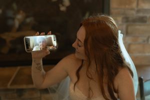 A bride in a white dress shows her phone screen while sitting at the reception.