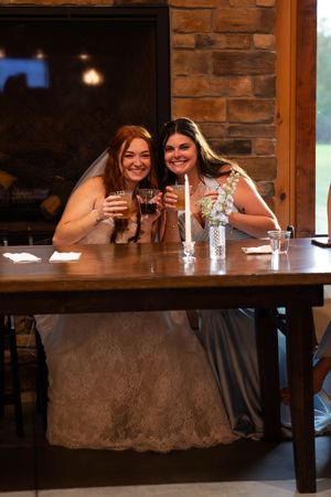 Wedding party members enjoying drinks at a rustic wooden bar with brick walls.