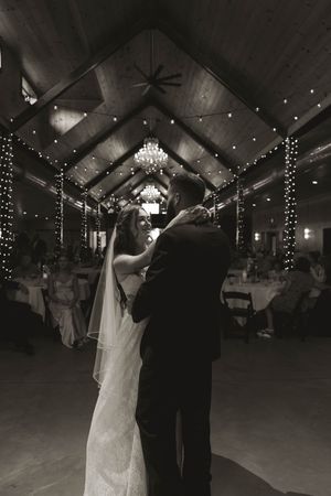 First dance at wedding reception under crystal chandeliers and string lights.