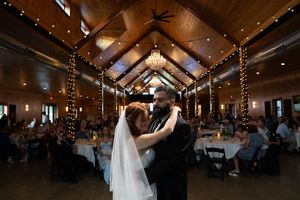Wedding reception dance floor with elegant lighting and rustic wooden ceiling beams.