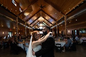 Couple dancing beneath twinkling lights and wooden beams at their wedding reception.