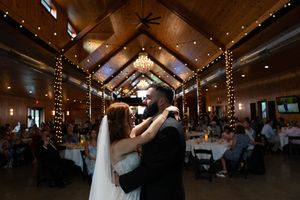 Couples dancing beneath string lights and chandeliers at rustic wedding venue.