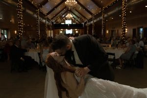 Wedding guests dance and celebrate under ornate chandeliers in a rustic barn reception space.