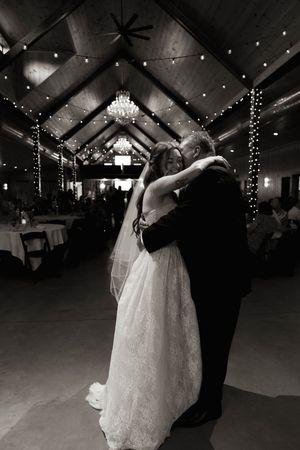 A bride in a white gown dances with her partner under elegant string lights and chandeliers.