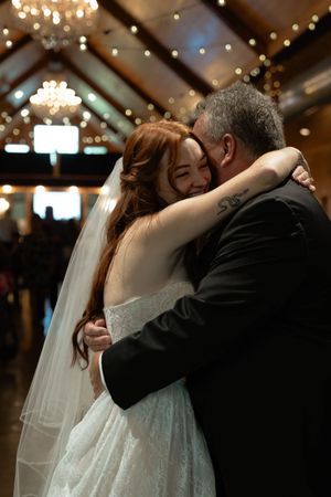 A couple embraces during their wedding dance beneath crystal chandeliers and string lights.