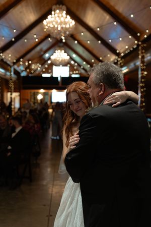 A tender dance moment unfolds beneath elegant lighting in a rustic reception venue.