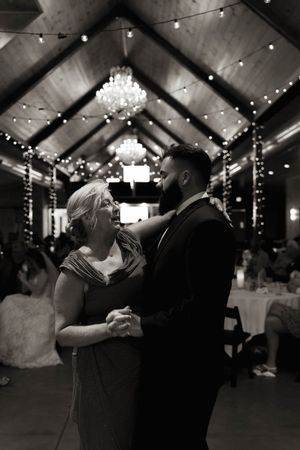 A couple shares an intimate dance moment under twinkling lights at an indoor wedding venue.