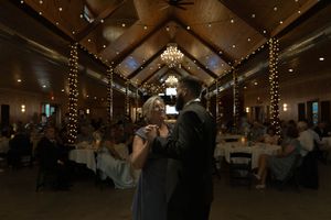A festive wedding reception takes place in a barn venue adorned with chandeliers and string lights.