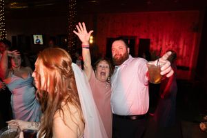 Energetic wedding reception scene with guests dancing and celebrating under red lighting.
