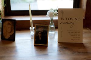 Memorial display with framed photos, candles and 'In Loving Memory' sign on wooden table.