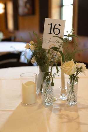 Elegant table setting with number 16 card, white roses in crystal vases and a pillar candle.