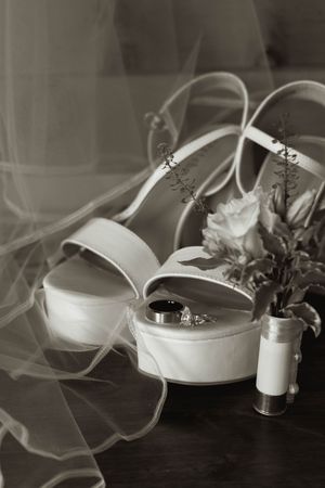 Black and white photo of bridal shoes with veil and flowers on wooden surface.