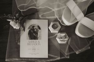 Black and white photo of wedding details including invitation, ring box, and bridal accessories.
