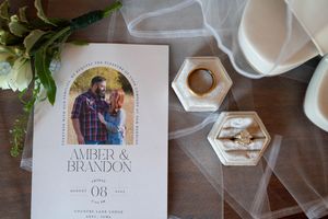 Wedding invitation with hexagonal ring box and white platform shoes on wooden surface.