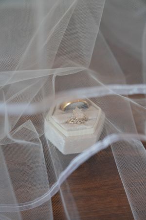 Delicate white tulle veil draped over wedding accessories on a dark wooden surface.