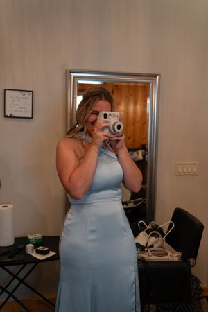 Someone in a light blue bridesmaid dress takes a photo with an instant camera in a getting ready room.